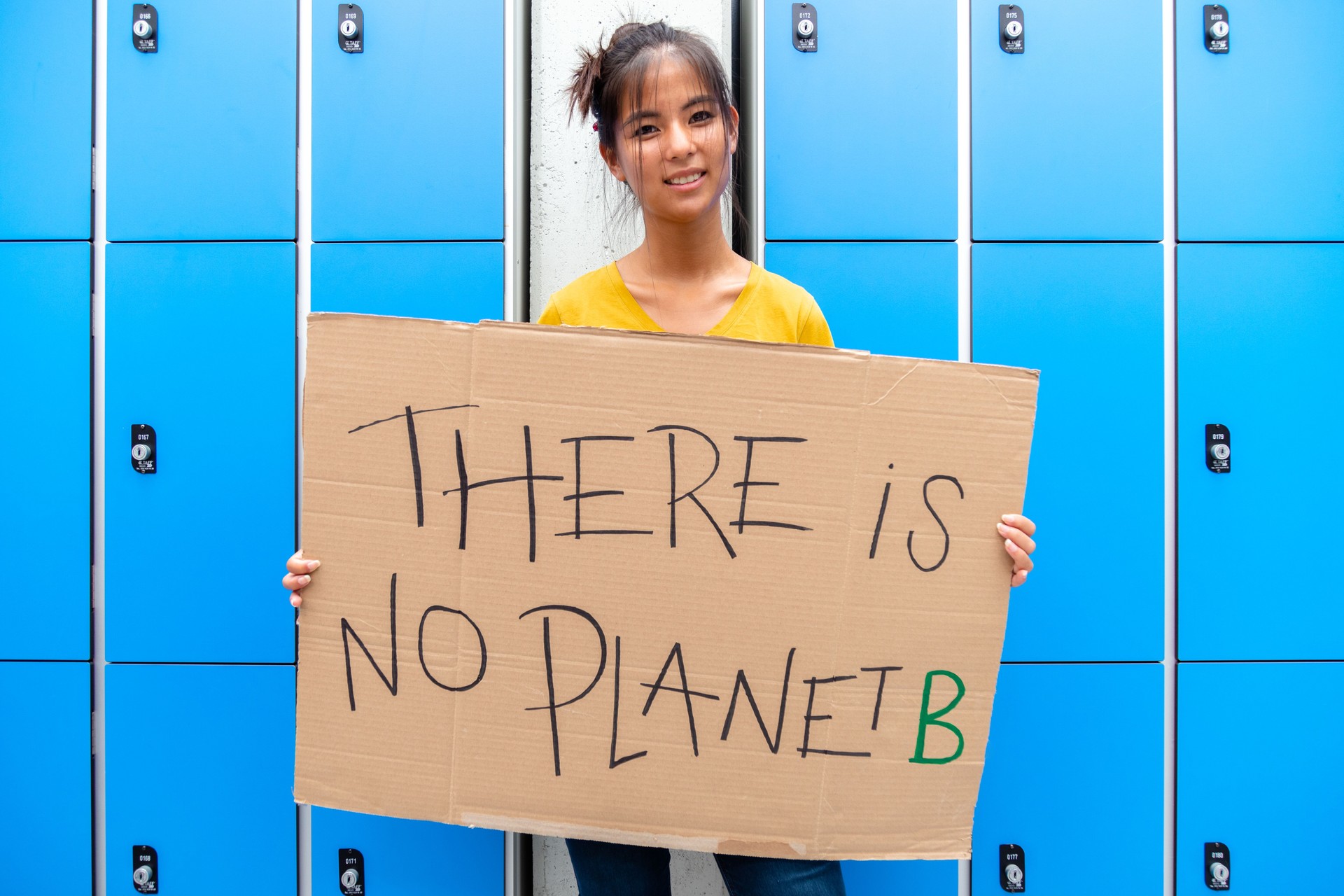 Teen asian high school girl student looking at camera carrying a vindictive "there is no planet b" placard.