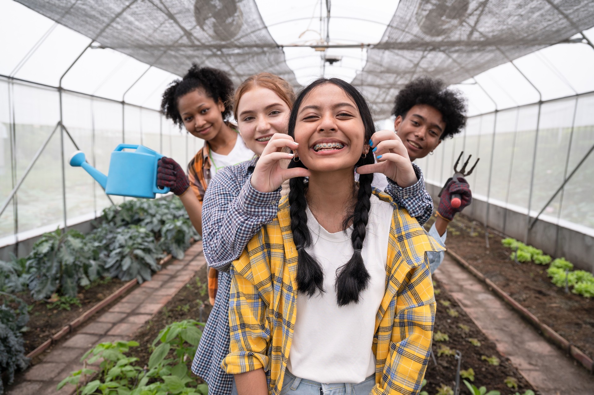 Mix race teenagers holding farmer tool in organic greenhouse